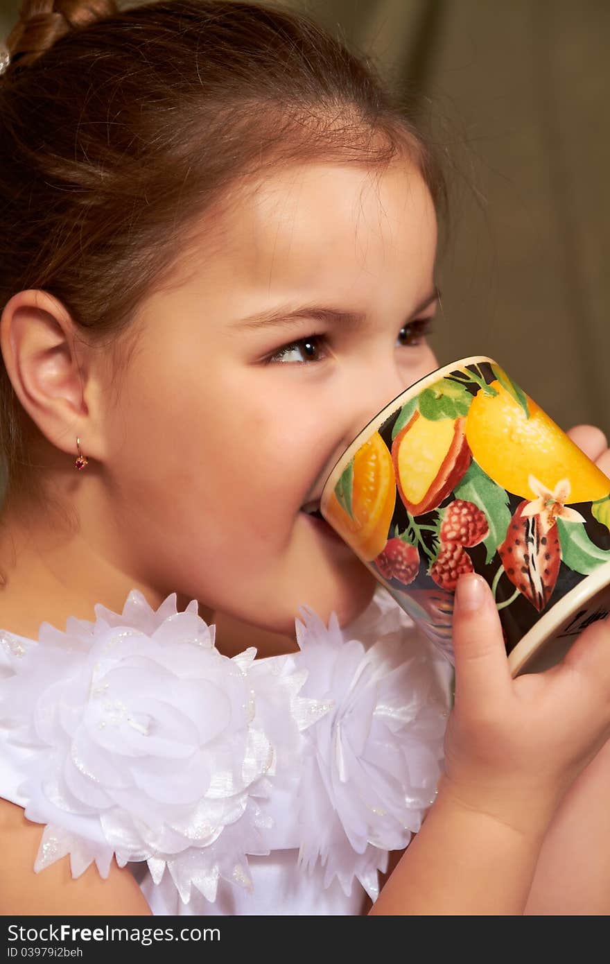 The little girl in a white dress drinks from a large mug. The little girl in a white dress drinks from a large mug.