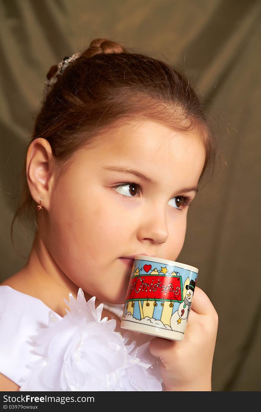 The little girl in a white dress drinks from a small cup. The little girl in a white dress drinks from a small cup.