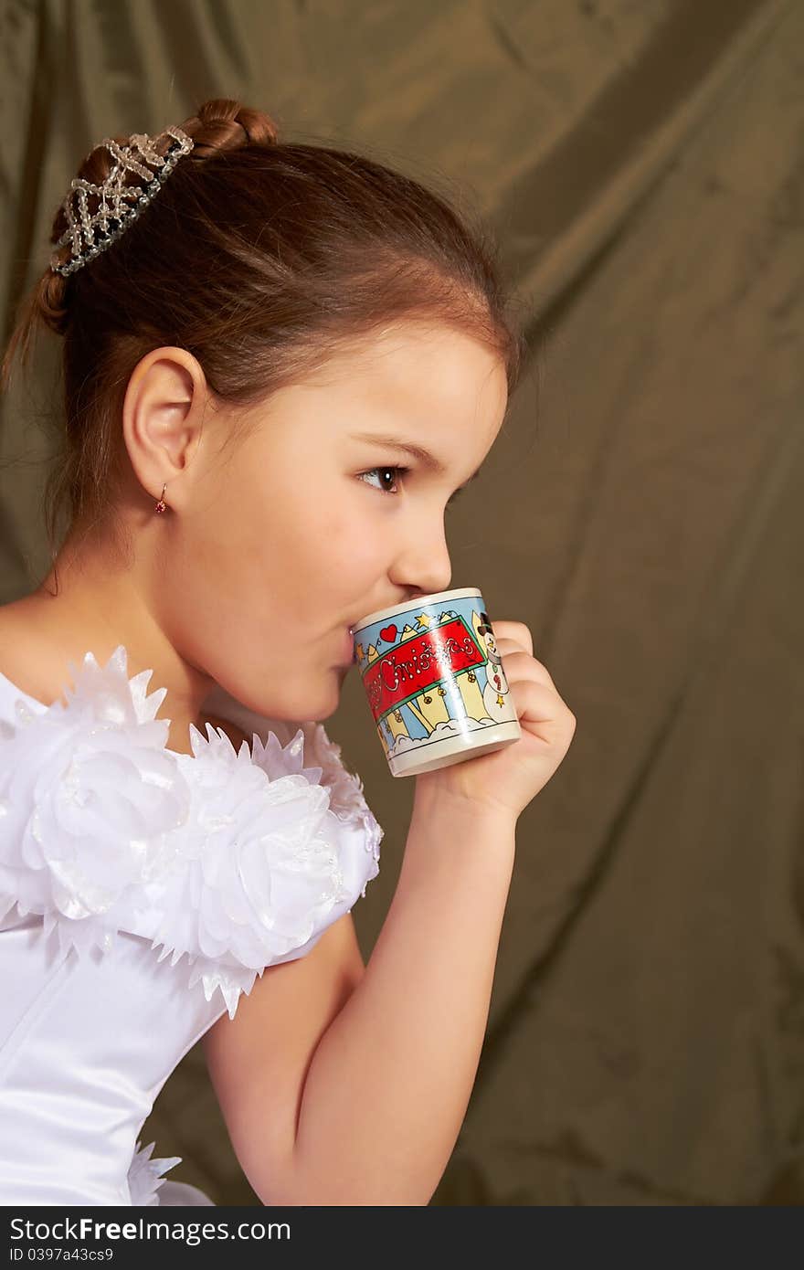 The little girl in a white dress drinks from a small cup. The little girl in a white dress drinks from a small cup.