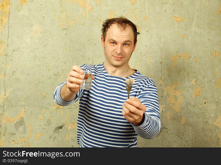 Man on the background of the old concrete wall keeps drinks vodka and pickles. On a man wearing vest. USSR. Man on the background of the old concrete wall keeps drinks vodka and pickles. On a man wearing vest. USSR