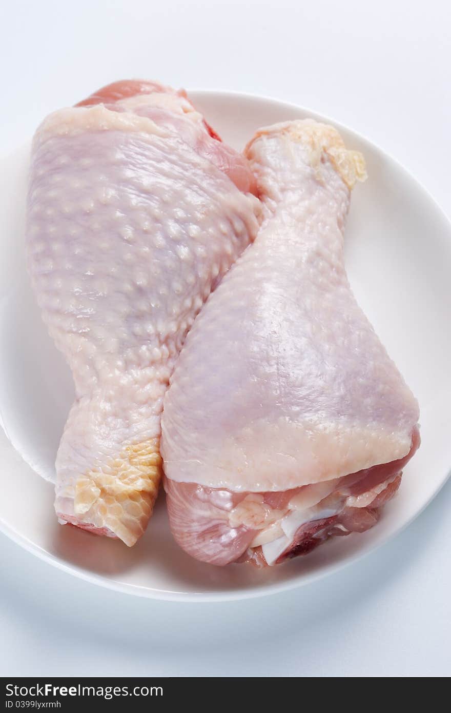 Two raw chicken legs on a plate on a white background