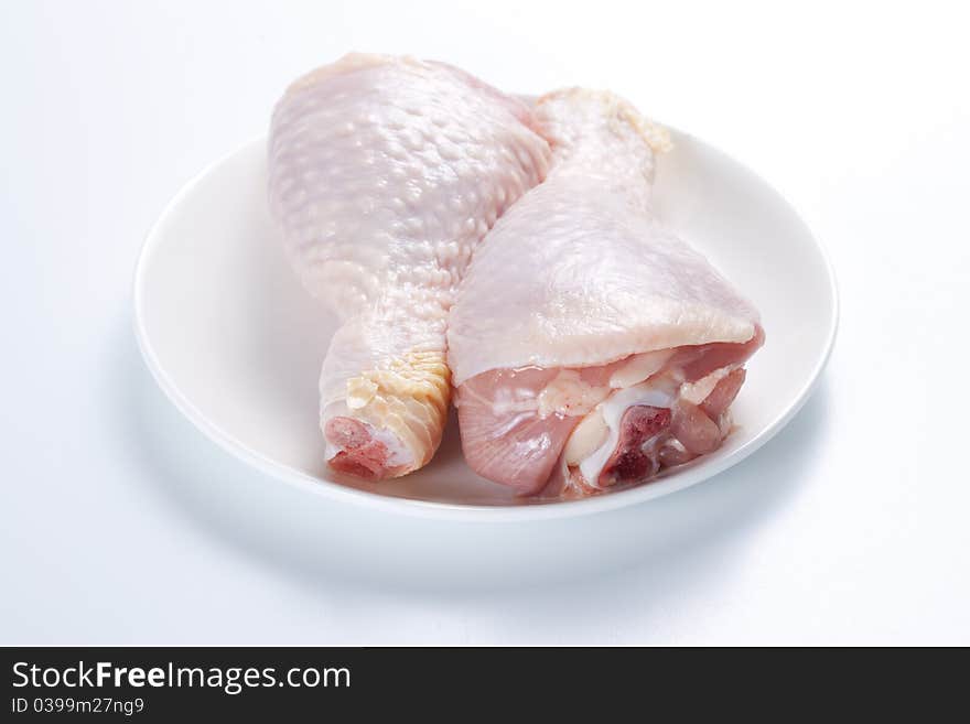 Two raw chicken legs on a plate on a white background