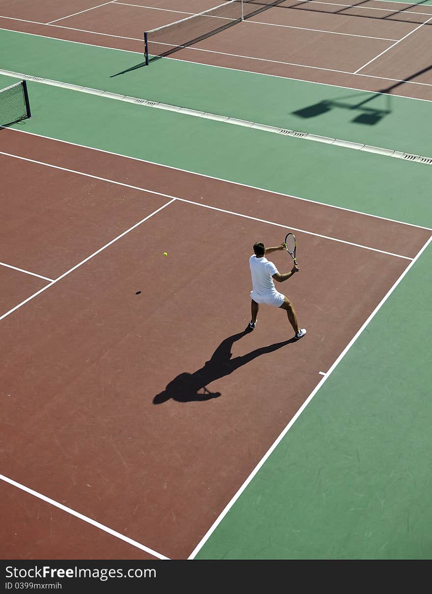 Young man play tennis outdoor on orange tennis field at early morning