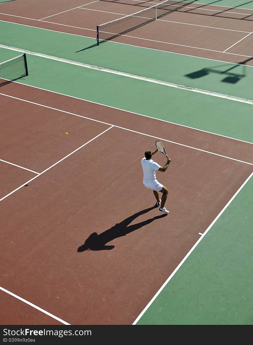 Young man play tennis outdoor on orange tennis field at early morning