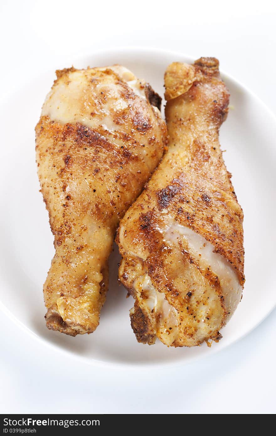 Two roasted chicken legs on plate on white background