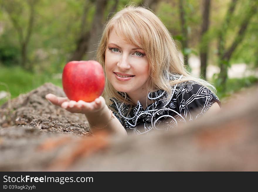 Beautiful smiling young woman with red apple in her hand outdoors, spring day