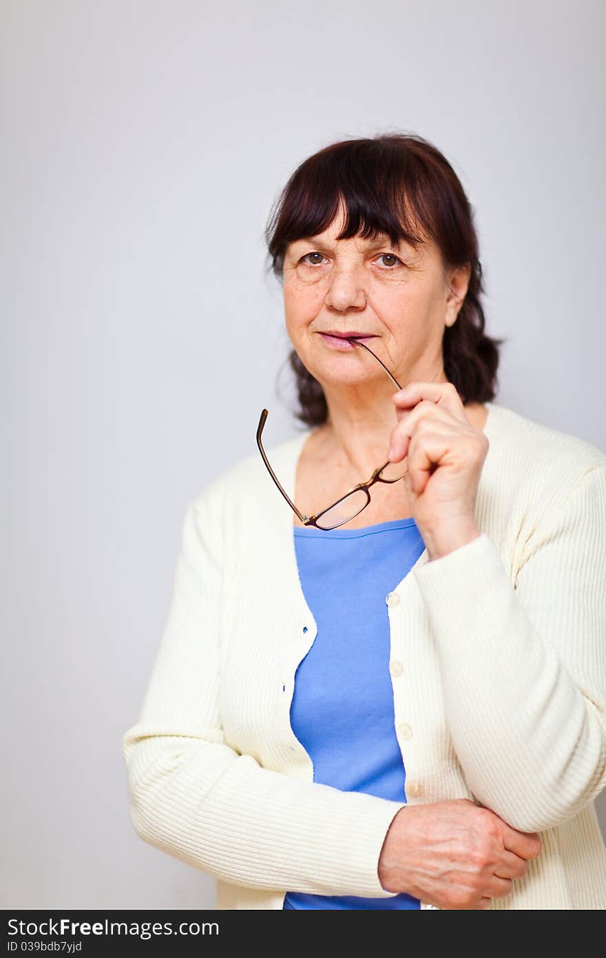 Senior woman standing at the wall holding her glasses and looking into the camera. Senior woman standing at the wall holding her glasses and looking into the camera