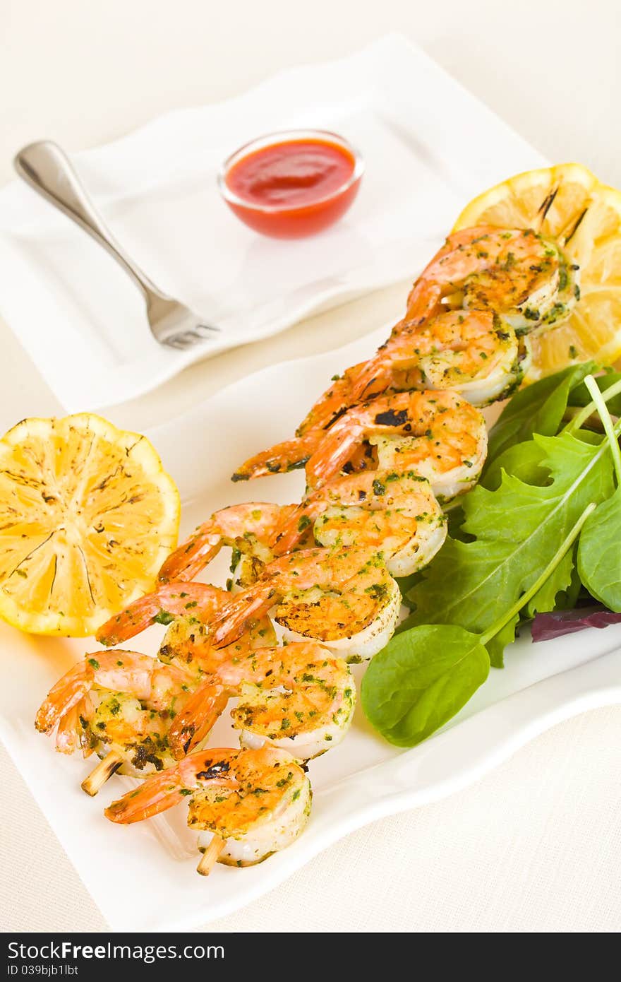 Fresh shrimp skewers on a white plate with citrus, salad and seafood sauce. Shallow depth of field. Fresh shrimp skewers on a white plate with citrus, salad and seafood sauce. Shallow depth of field.