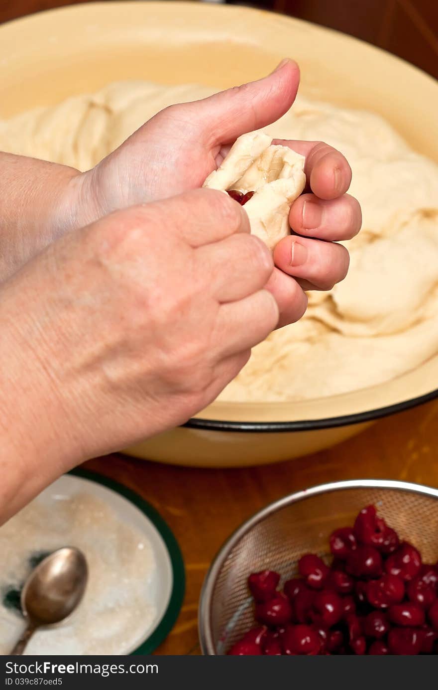 Female hands making small pies with cherry on a table. Female hands making small pies with cherry on a table