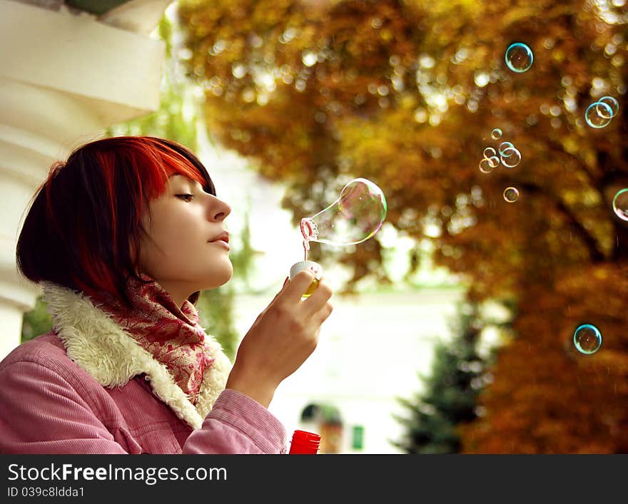 A girl is in an autumn park blowing a soap-bubbles