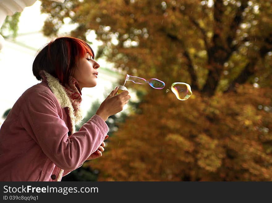 A girl is in an autumn park blowing a soap-bubbles