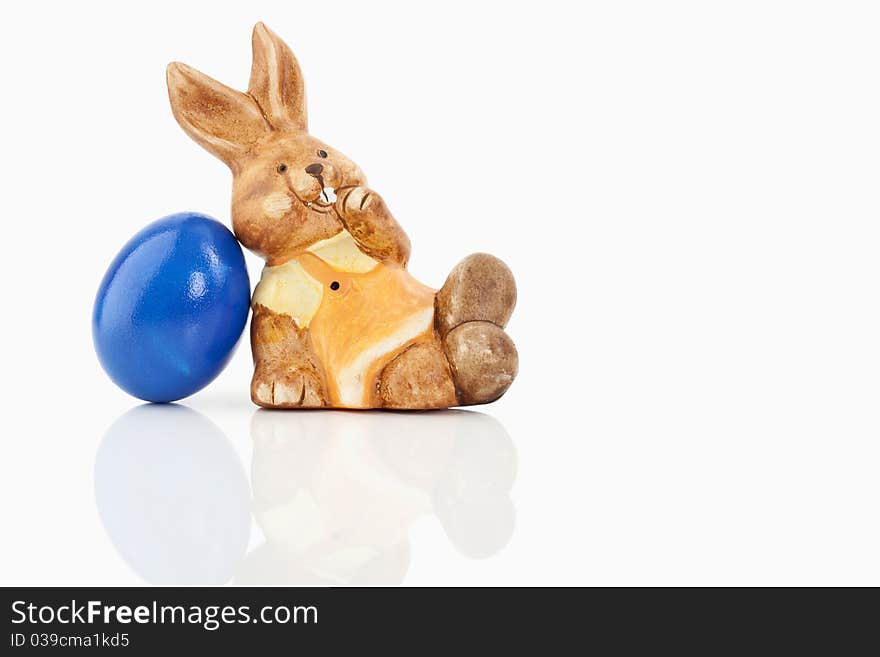Easter bunny sitting close to a blue egg on a white background
