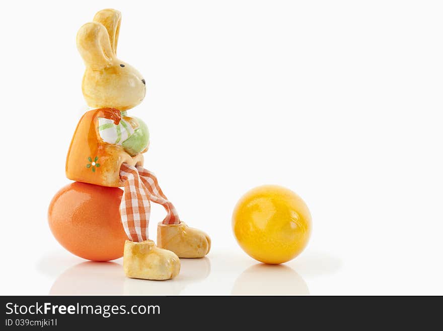 Easter bunny sitting on an orange egg close to a yellow egg on a white background