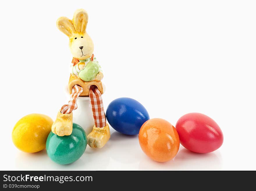 Easter bunny sitting on an egg-cup close to colored eggs on a white background