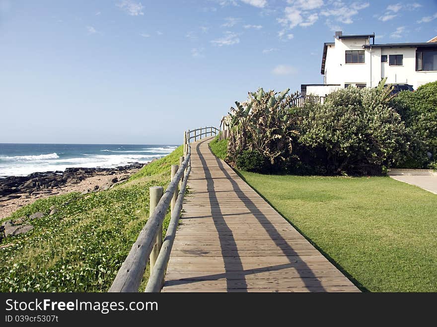 A wooden walkway with a handrail next to a bech. A wooden walkway with a handrail next to a bech