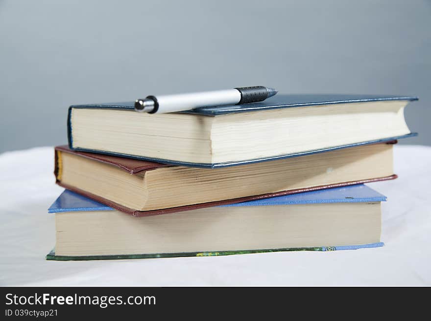 Pen lies on a pile of books on a gray background. Pen lies on a pile of books on a gray background