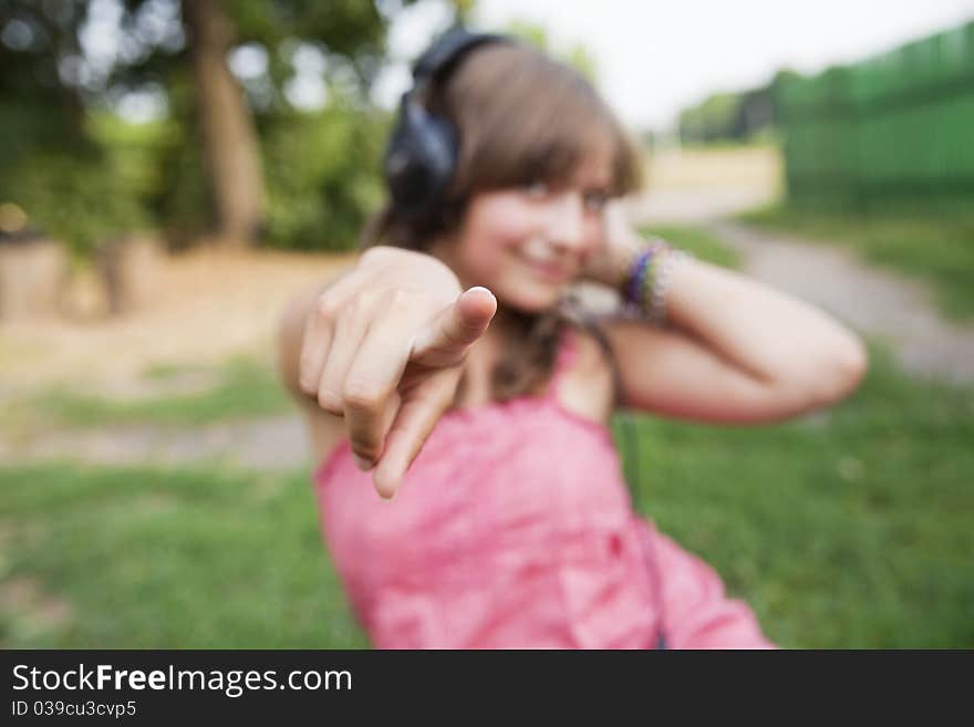 Beautiful teenage girl in a pink dress with headphones to point the finger at the camera, focus on finger. Beautiful teenage girl in a pink dress with headphones to point the finger at the camera, focus on finger