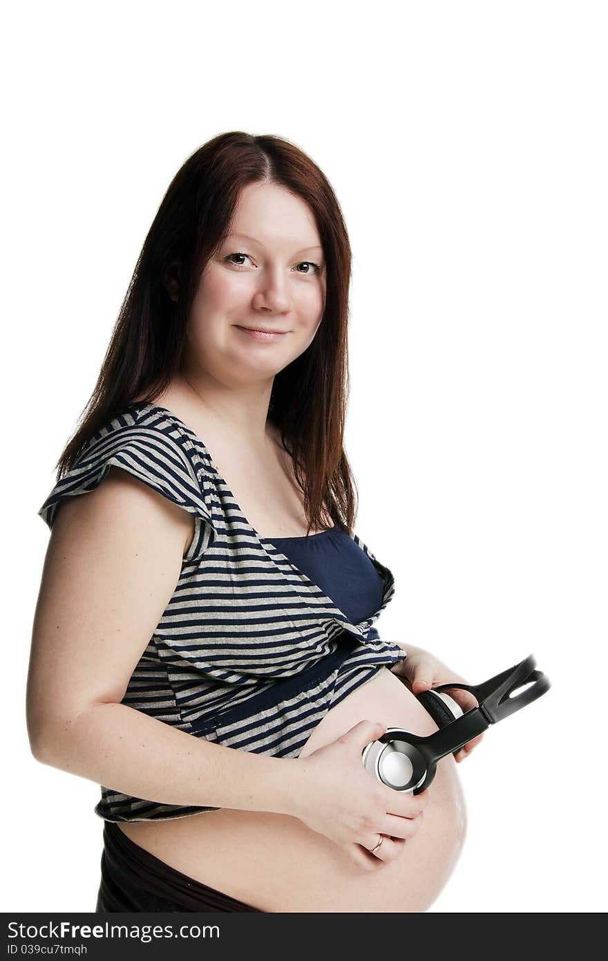 Green-eyed smiling pregnant woman holding headphones about the stomach, isolated on white