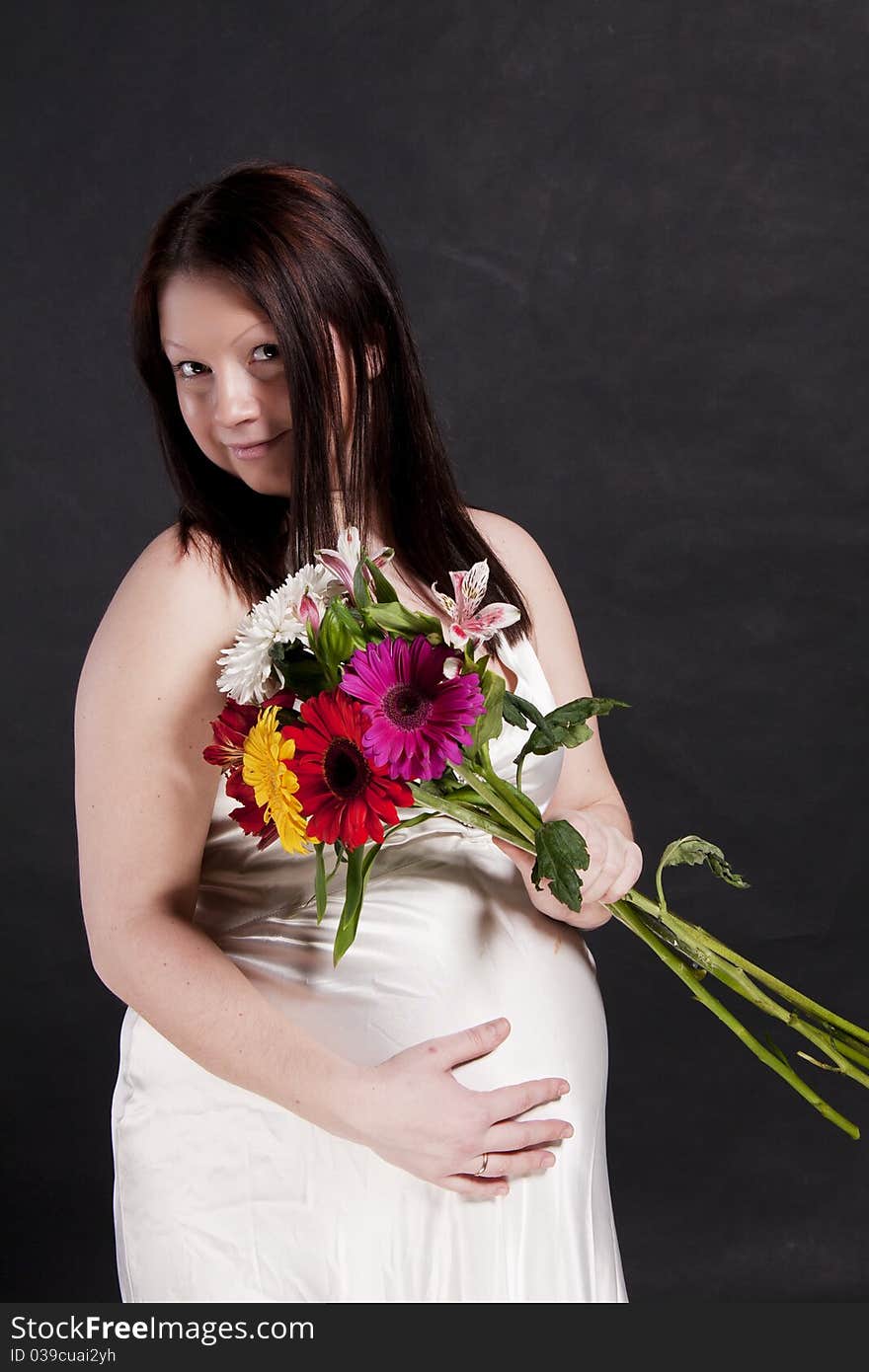 Pregnant woman in white dress with gerbera bouquet