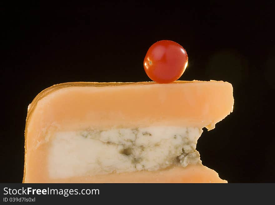 Gloucester cheese with Cheese blue slice on a black background with tomato. Gloucester cheese with Cheese blue slice on a black background with tomato.