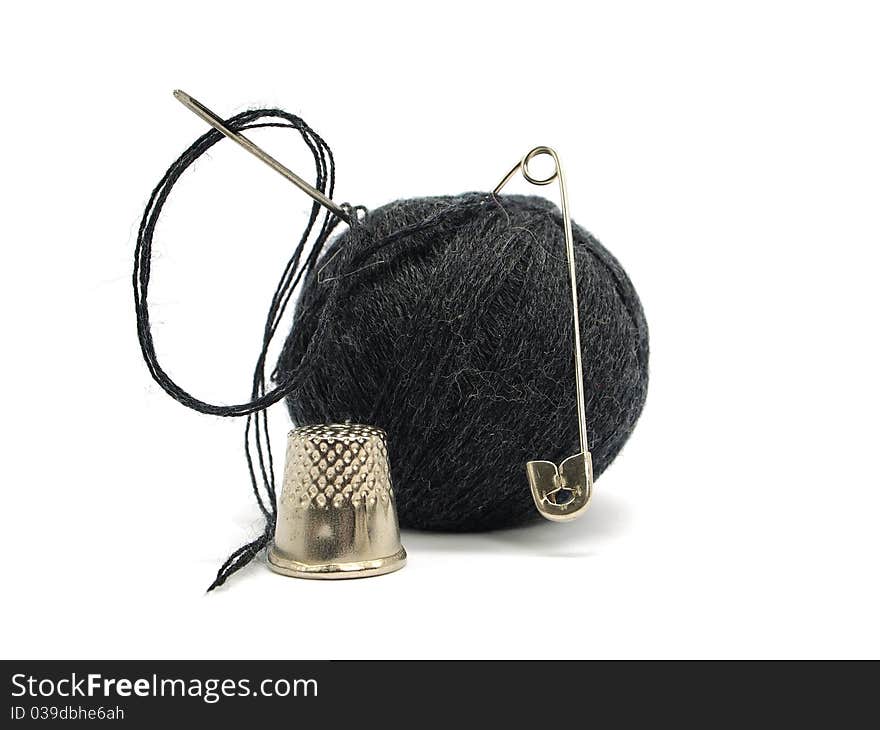 Black thread ball, pin, thimble and needle on a white background