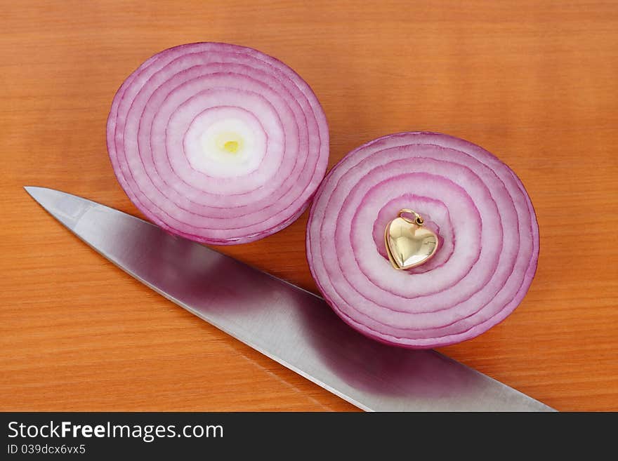 Two red onion halves, kitchen knife and golden heart on the kitchen board. Two red onion halves, kitchen knife and golden heart on the kitchen board