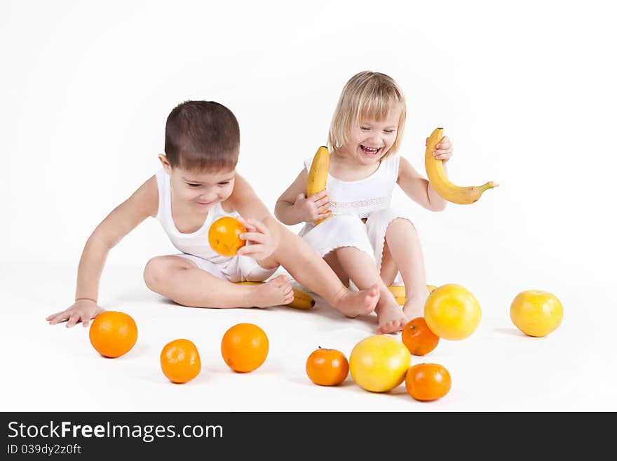 Cute baby girl and baby boy play with fruits over white. Cute baby girl and baby boy play with fruits over white