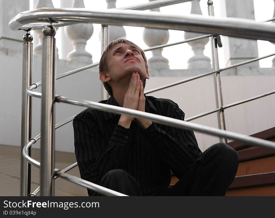 A young man in a black shirt sitting on the stairs and asks for help sky