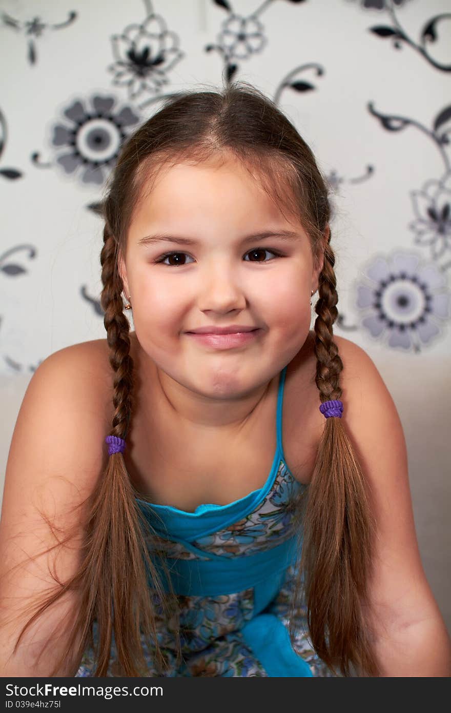 A smiling little girl in a blue dress and pigtails on the head.