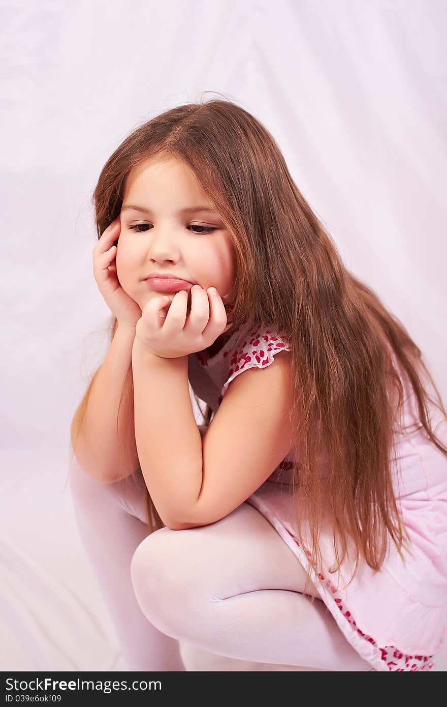 A girl sits upset and thinking about pressing issues on a white background, white tights and white-pink dress. A girl sits upset and thinking about pressing issues on a white background, white tights and white-pink dress.