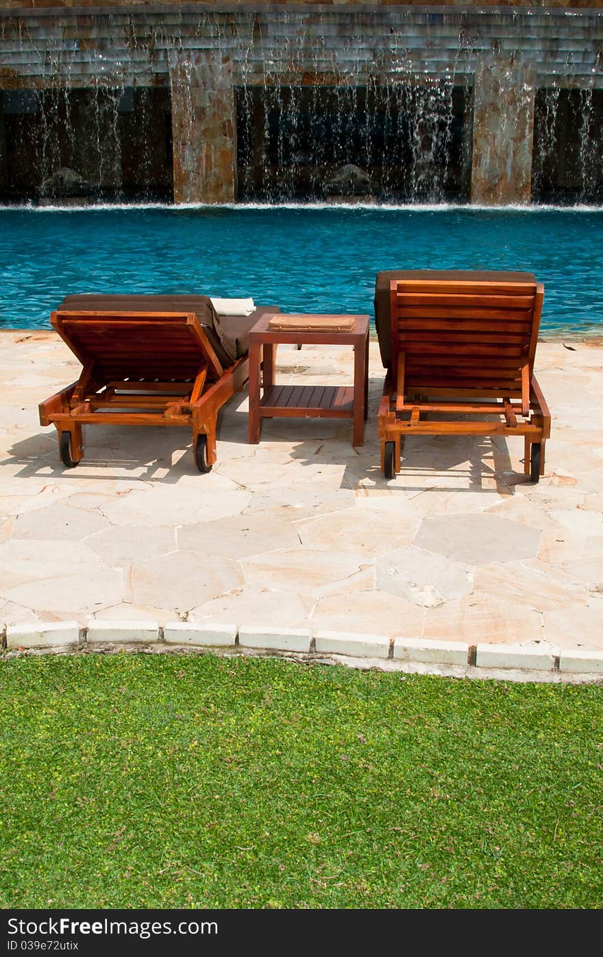 A portrait of tropical swimming pool setup with chairs, towers, greenery and waterfall