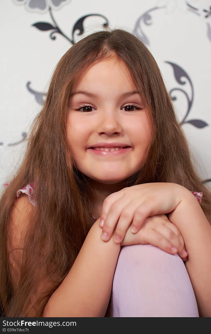 The little girl is sitting, smiling, his hands placed on the knee. The little girl is sitting, smiling, his hands placed on the knee.