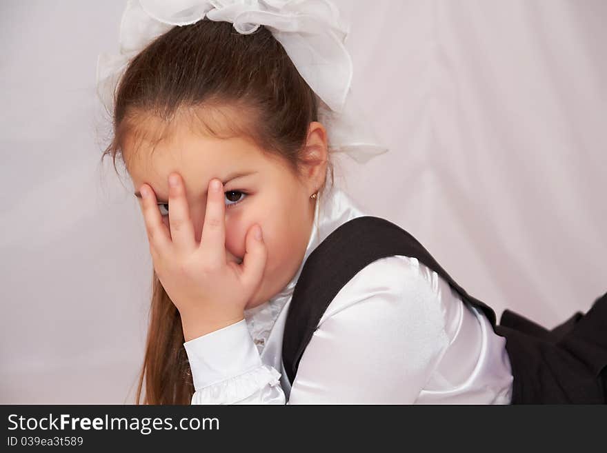 The little girl in school uniform lying and covers his face with his fingers. The little girl in school uniform lying and covers his face with his fingers.