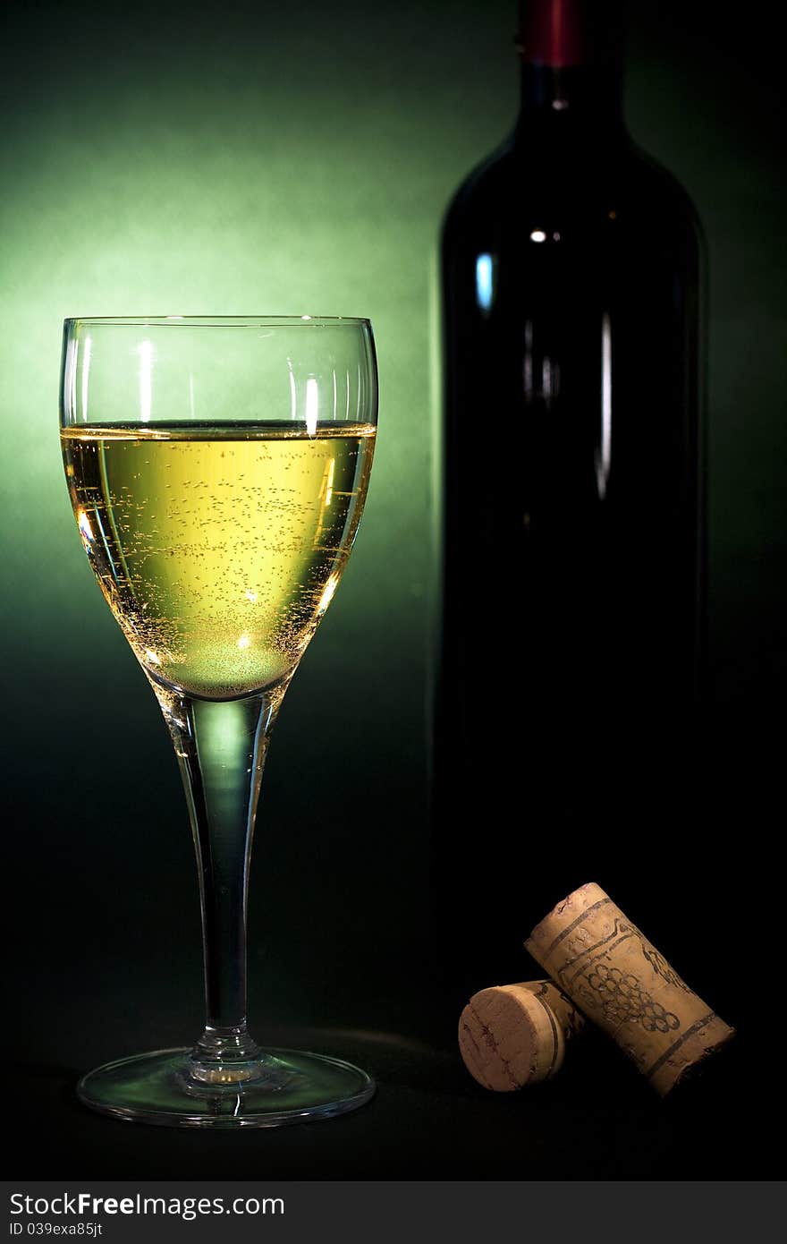 Crystal wine glass with white wine and a bottle, on black background with green gel, Luxury art background for beverages (part of collection)