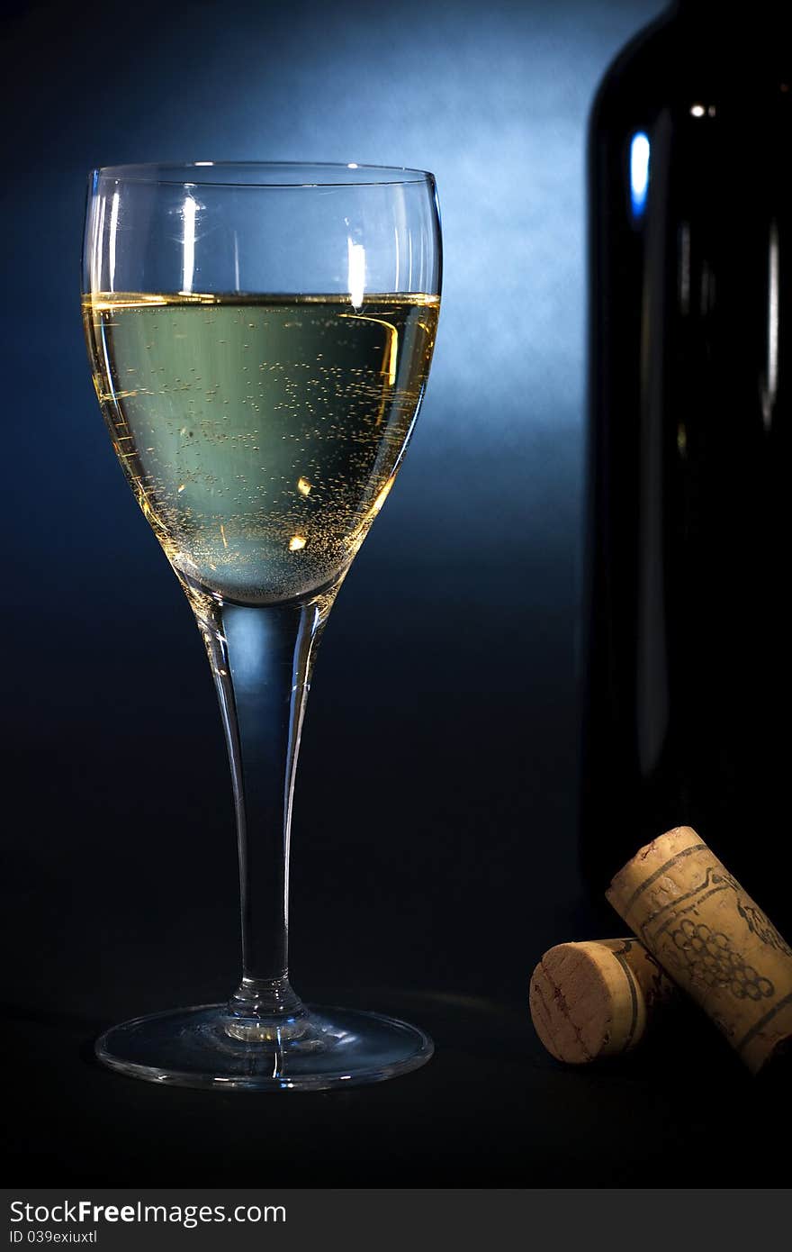 White wine in a glass closeup & a bottle, on black-blue background. Art heme. White wine in a glass closeup & a bottle, on black-blue background. Art heme