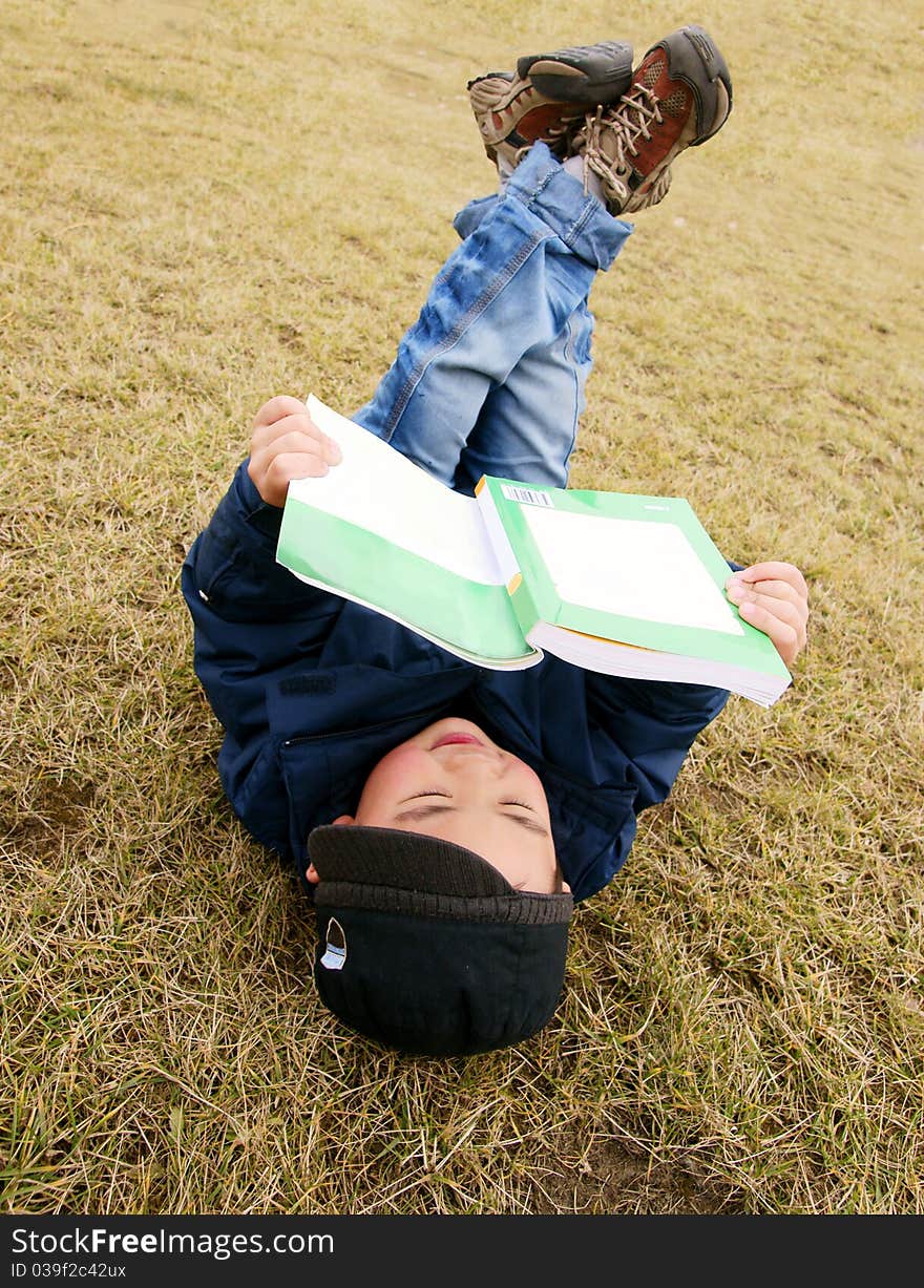 Picture of a little chinese boy reading a book while lying on the garden lawn in the spring sunshine. Picture of a little chinese boy reading a book while lying on the garden lawn in the spring sunshine