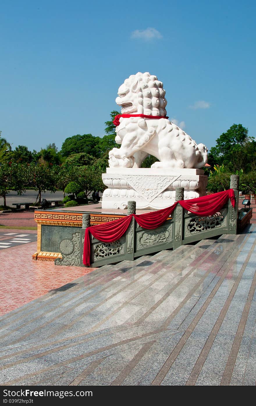 A stone lion outside the temple with a foreground of marble steps and a lush greenery at the background. A stone lion outside the temple with a foreground of marble steps and a lush greenery at the background