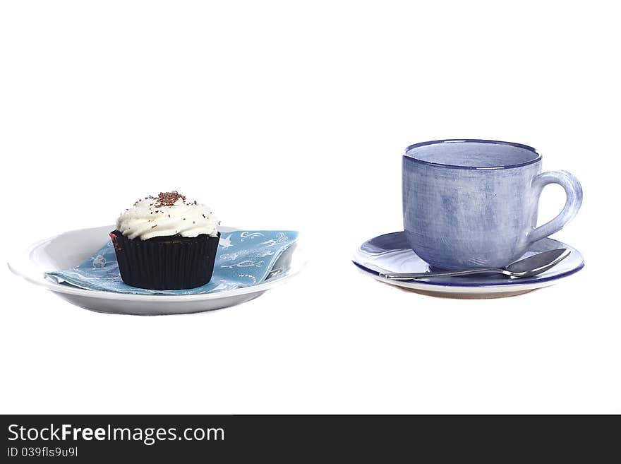 Pottery cup and saucer alongside schocolate cupcake with cream icing. Pottery cup and saucer alongside schocolate cupcake with cream icing