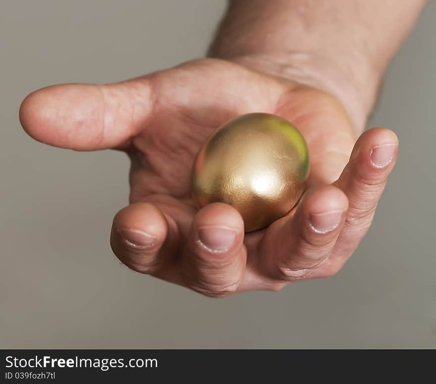 The man holds in a hand gold egg as a symbol of financial success. The man holds in a hand gold egg as a symbol of financial success