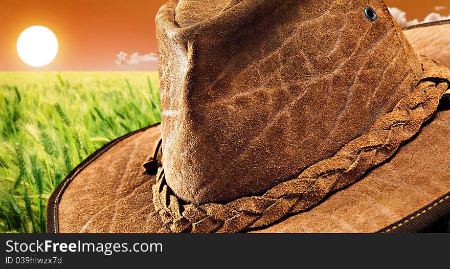 Close up of a leather hat made of crocodile skin with beautiful sunset over a wheat field in the background