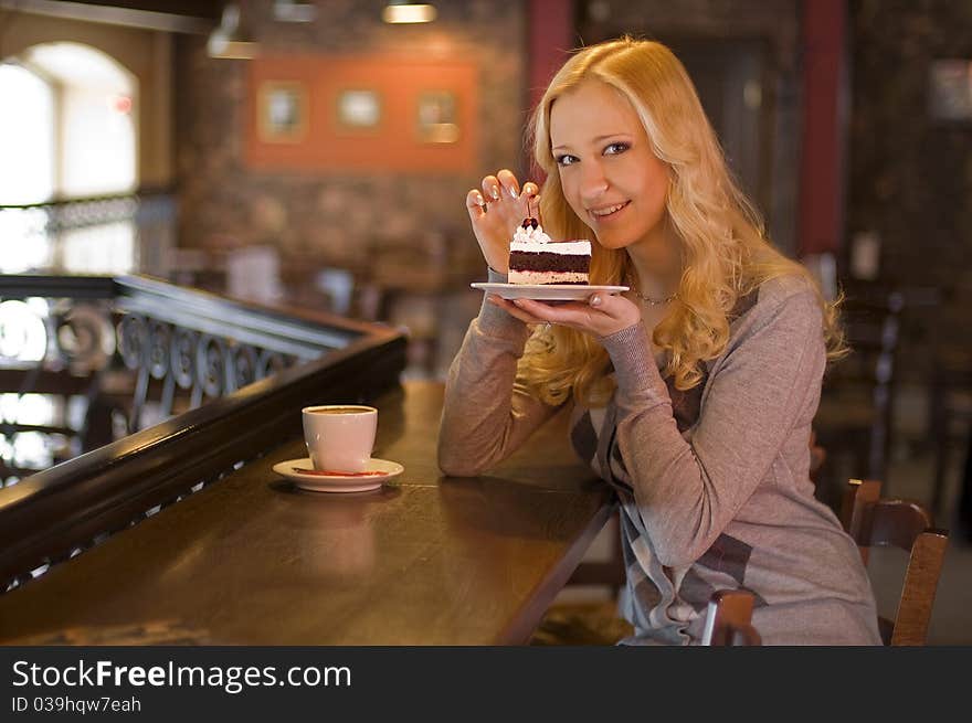 The charming girl drinks coffee with a cake in cafe