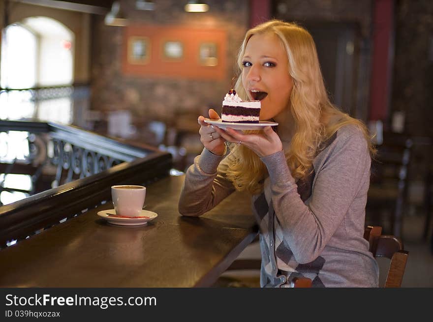 The charming girl drinks coffee with a cake in cafe