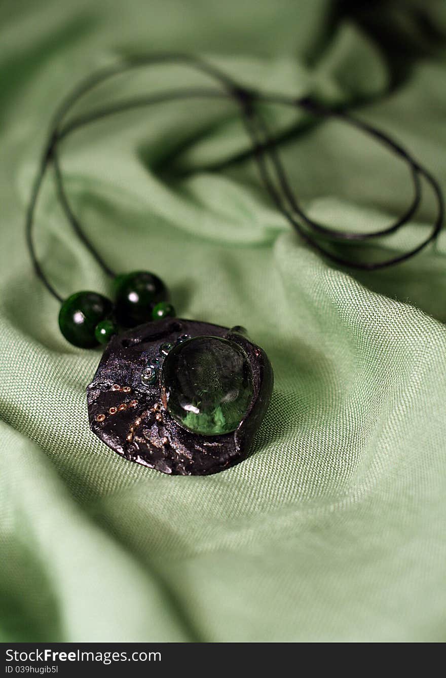 A green handmade pendant laying on a green satin scarf. A green handmade pendant laying on a green satin scarf