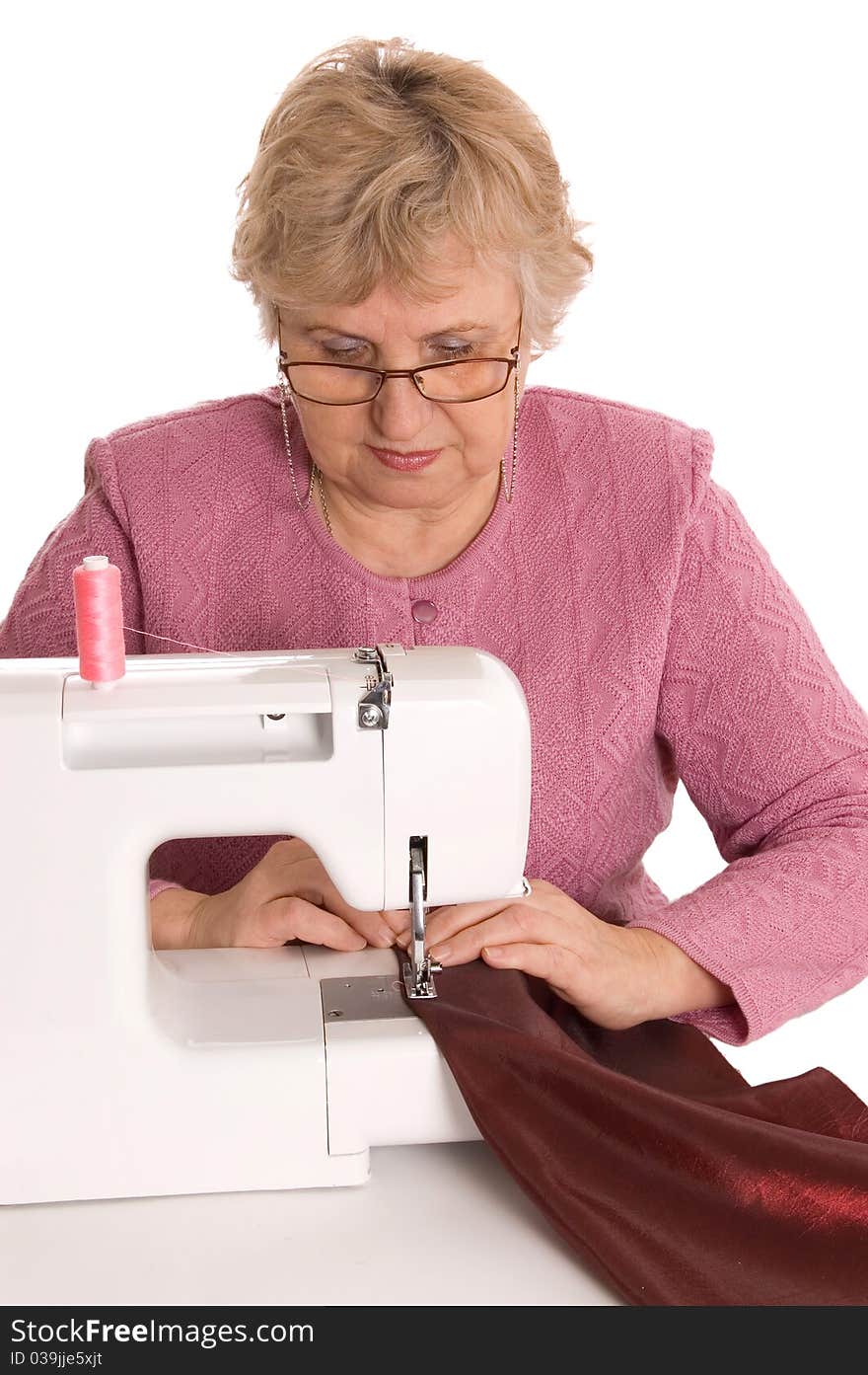 The elderly woman sews on the sewing machine on white