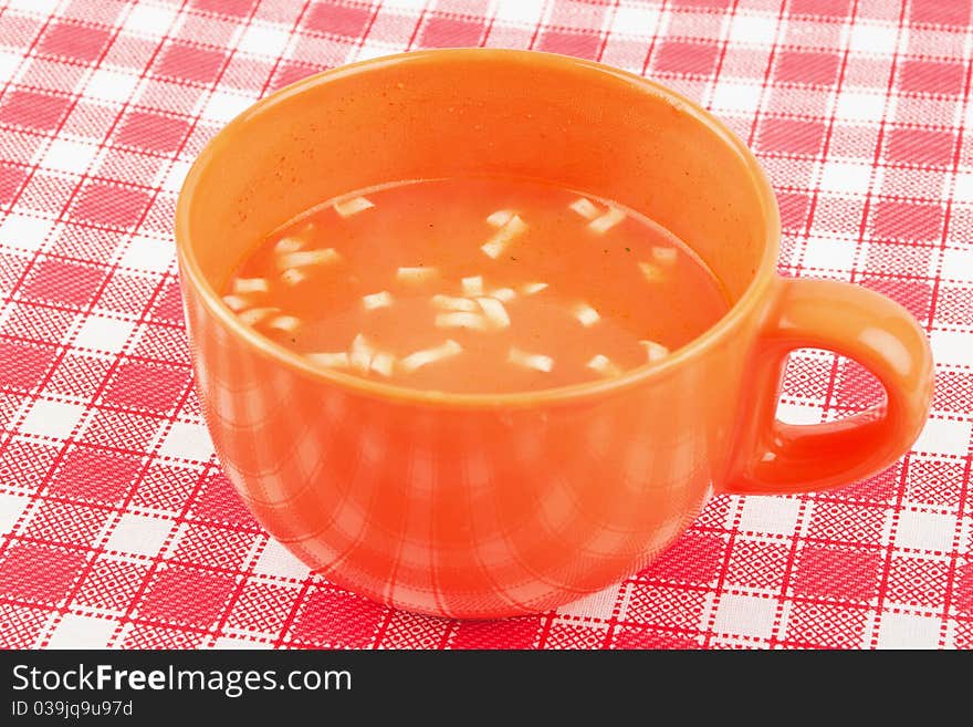 Orange bowl of tomatoes soup on red and white table cloth