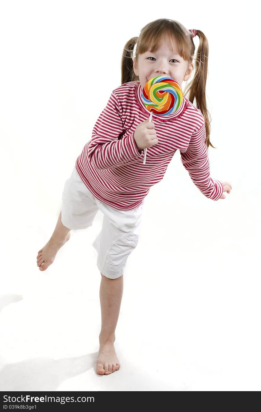 Dancing little girl eatis a lollipop isolated on white