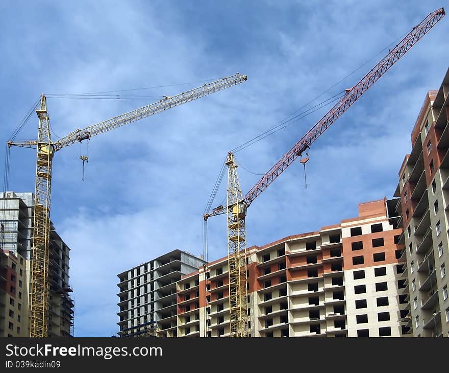 Under construction apartment house and two lifting cranes against a background of blue sky. Under construction apartment house and two lifting cranes against a background of blue sky