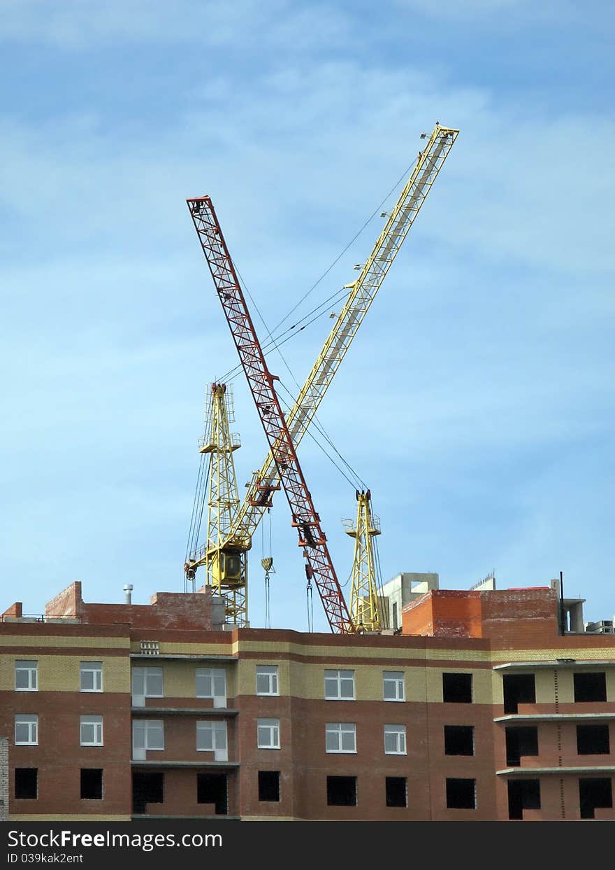 Under construction apartment house and two lifting cranes against a background of blue sky. Under construction apartment house and two lifting cranes against a background of blue sky