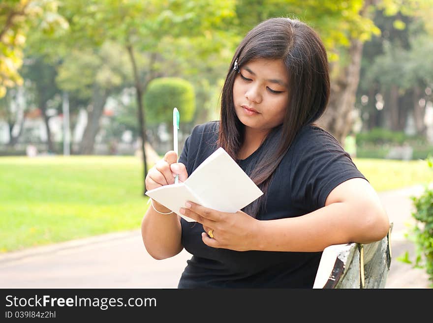 Women sitting in the park and is writing a notebook in it. Women sitting in the park and is writing a notebook in it.