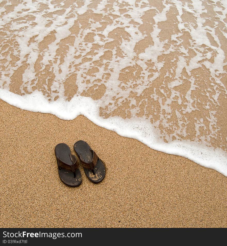 Beach sandles or tongs on a sandy beach with lots of background copyspace